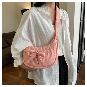 Pink nylon crossbody bag detail with large decorative bow on model in home setting