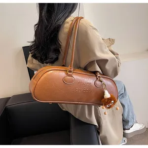Detail of dark brown cylindrical leather bag with logo embossing and plush charm