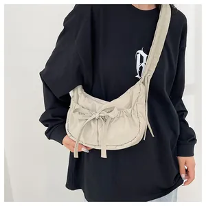 Close-up of beige crescent crossbody bag featuring drawstring bow and pleated nylon texture