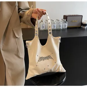 Dettaglio borsa tote crema con logo punk argento e manici con occhielli in metallo