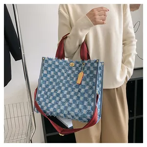 Detailed close-up of large denim checkerboard tote bag with stylish frayed edges and red straps