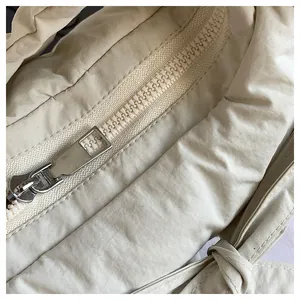 Close-up of smooth metal zipper and quilted nylon texture on cream-colored tote bag