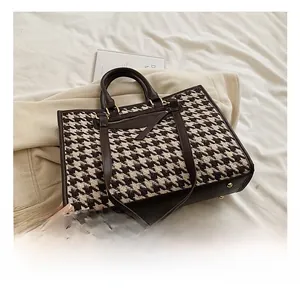 Close-up of houndstooth tote bag with brown leather handles and gold metal studs