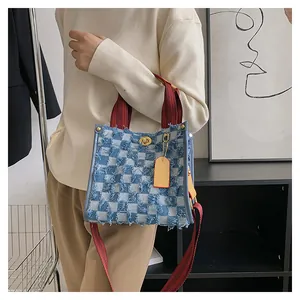 Detail of blue checkerboard denim tote bag with frayed edges and brown striped handle