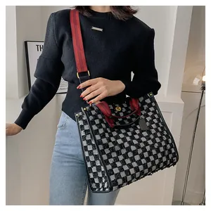 Detail of checkered denim tote bag with red handles and adjustable woven strap