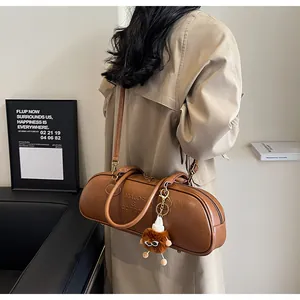 Brown leather baguette bag featuring a plush charm and brand embossing on the side