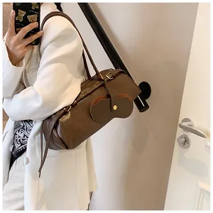 Detail of dark brown leather cylindrical bag with metal eyelets and decorative charm