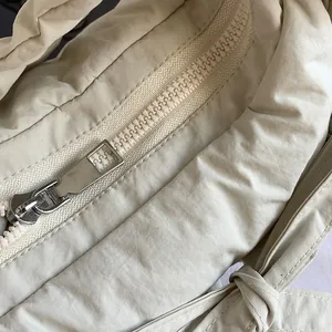 Minimalist beige nylon crossbody bag featuring drawstring knot details and silver metal zipper