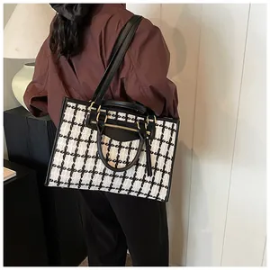 Detailed view of houndstooth tote bag with gold hardware and adjustable strap on a model