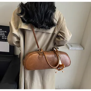 Retro brown cylinder bag with embossed letters and plush monster charm shown on model