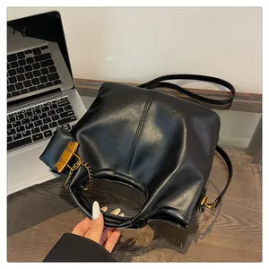 Detail of black PU leather bucket bag with gold chain and handle on wooden desk