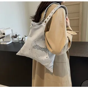 Dettaglio della borsa metallica argento con borchie ed emblema su cappotto beige
