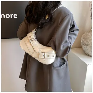 Detail view of cream shoulder bag with metallic eyelets and belts on a model