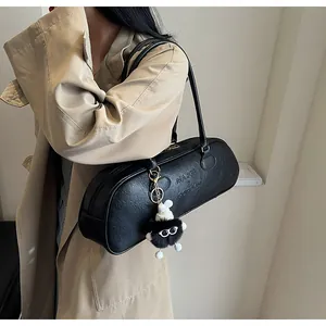 Close-up of a black textured leather cylinder shoulder bag with a plush monster charm