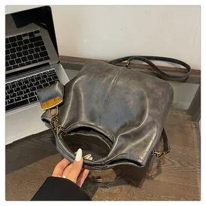 Detail view of charcoal grey leather bucket bag with retro metal buckle and chain on desk
