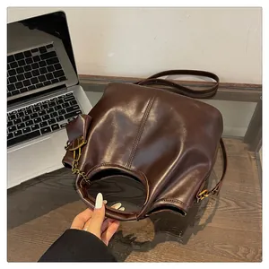 Detailed view of dark brown leather bucket bag with cut-out handle on glass desk