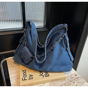 Detail of blue denim tote bag with metal chain strap and mini pouch on stone surface