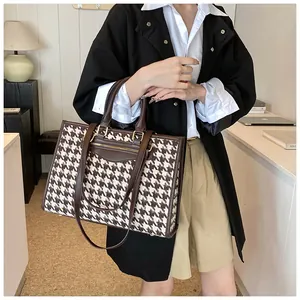 Detail view of houndstooth tote bag with dual handles and metal zipper in office setting