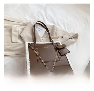 Brown leather tote with white faux shearling trim and decorative gold chain accent