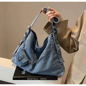 Detail of blue denim hobo bag featuring silver chain decor and mini charm pouch