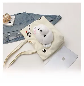 Detailed view of cream canvas tote bag with a 3D plush bear head and tablet for scale