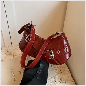 Detail of dark red patent leather shoulder bag with large silver buckle and grommet strap