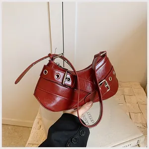 Detail of burgundy crescent shoulder bag featuring silver metal eyelets and belt straps