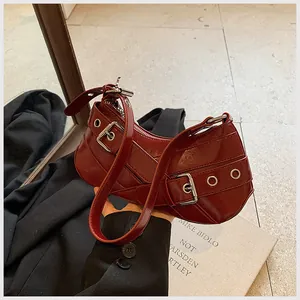 Detail of burgundy patent leather underarm bag featuring silver buckles and studs