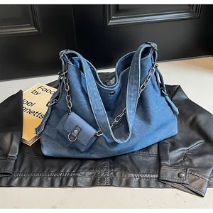 Detail of blue denim tote bag with metal chain and matching mini pouch on black leather