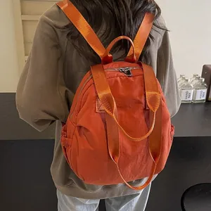 Caramel orange nylon backpack with minimalist design and top handle shown on a model