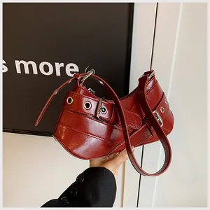 Detail of wine red glossy underarm bag featuring silver punk eyelets and buckles