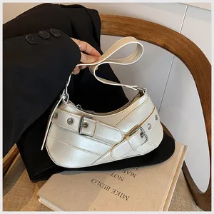 Detail of off-white faux leather crescent bag with buckle straps on a wooden chair