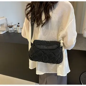 Close-up of a black quilted crossbody bag with rhombic pattern worn by a model
