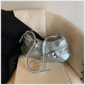 Detailed macro of silver metallic Y2K shoulder bag with buckles on a beige sofa