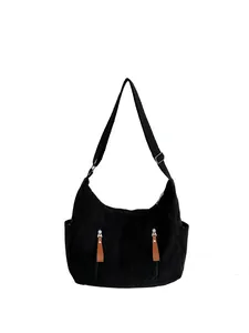 Detail of black corduroy dumpling bag with adjustable strap and decorative zipper pockets