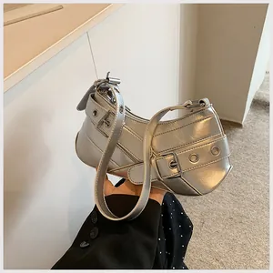 Detail of silver metallic underarm bag featuring multiple buckles and eyelet design