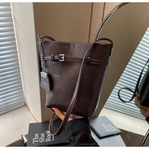 Detail of a brown leather bucket bag with silver metal chain and logo tag near a mirror