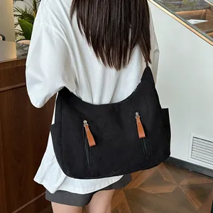 Large black corduroy dumpling crossbody bag with brown zippers shown in a cafe setting