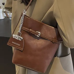 Brown leather bucket bag with metallic chain and shoulder strap in retro minimal style