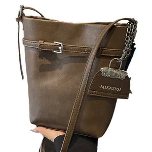 Dark brown leather bucket bag with silver metal buckle and crossbody strap on plain background