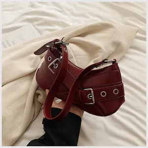 Macro detail of wine red underarm bag with punk buckled straps and silver eyelets