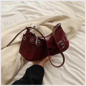 Detail view of burgundy underarm bag featuring decorative wide strap and metal eyelets