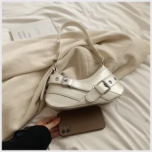 Detail of a creamy white crescent underarm bag with decorative metal eyelet straps