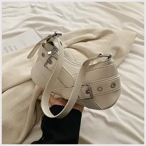 Detailed macro of a cream leather crescent shoulder bag featuring silver punk eyelets