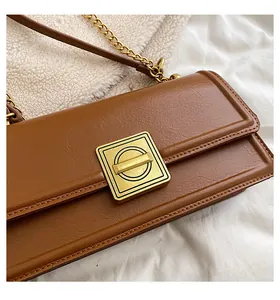 Close-up of brown textured leather square bag featuring a gold metal buckle and chain strap