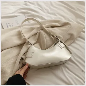 Detailed view of cream-colored minimalist underarm bag in glossy leather on white fabric