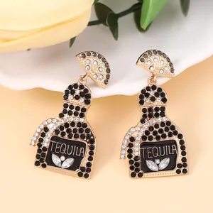 Detail of gold tequila bottle earrings with black and white rhinestones and lemon studs