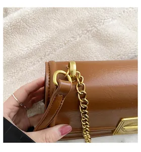 Detail of a brown leather square bag with gold D-ring hardware and chain strap attachment