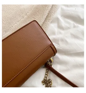 Detail shot of brown leather square bag showing golden chain and smooth stitching