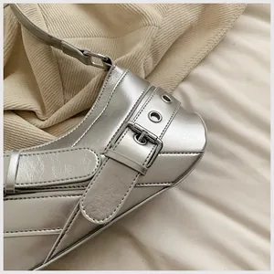 Close-up of metallic silver underarm bag with decorative buckles and stitching detail